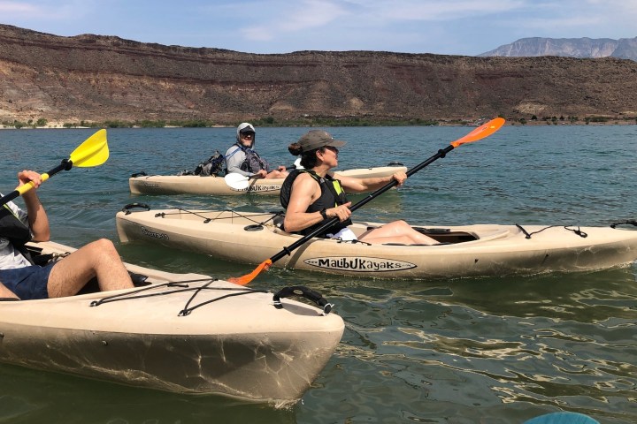 Three people kayaking on a lake with hills in the background.