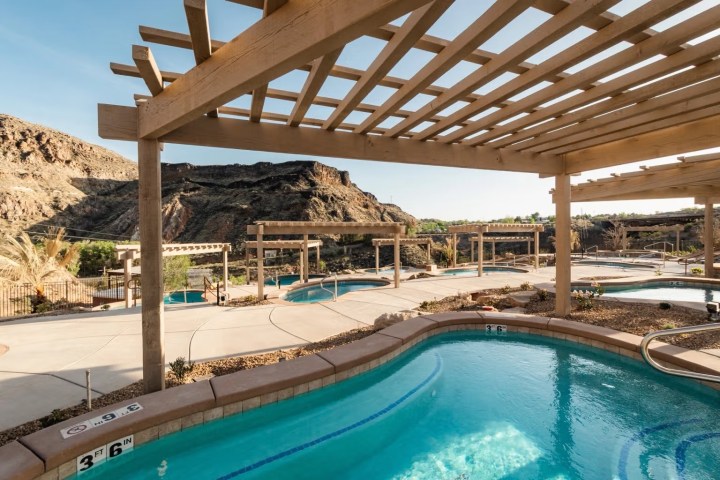 Outdoor pool area with pergolas and rocky landscape in the background.